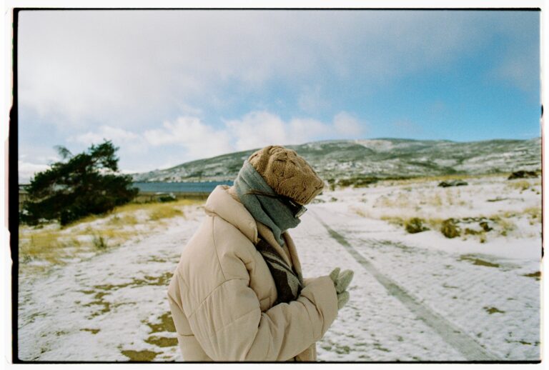 Person in winter clothing looking at phone on snowy path